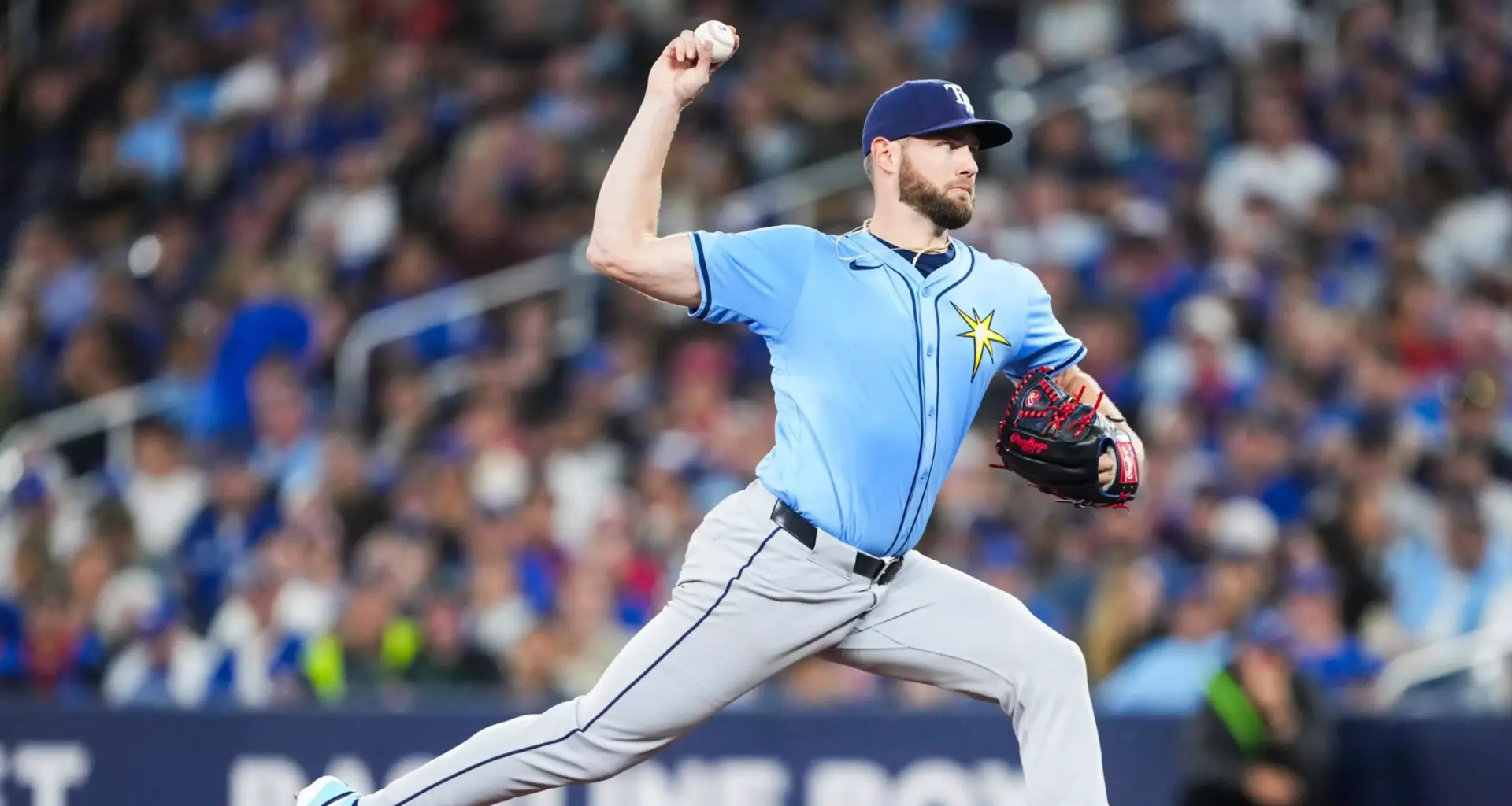 A football player in a red and gold uniform, holding a football, runs on a grassy field with a blurred crowd in the background.