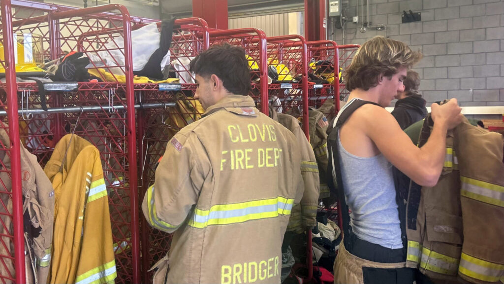 Image of two Clovis Unified male students donning firefighting gear in a lockerroom.