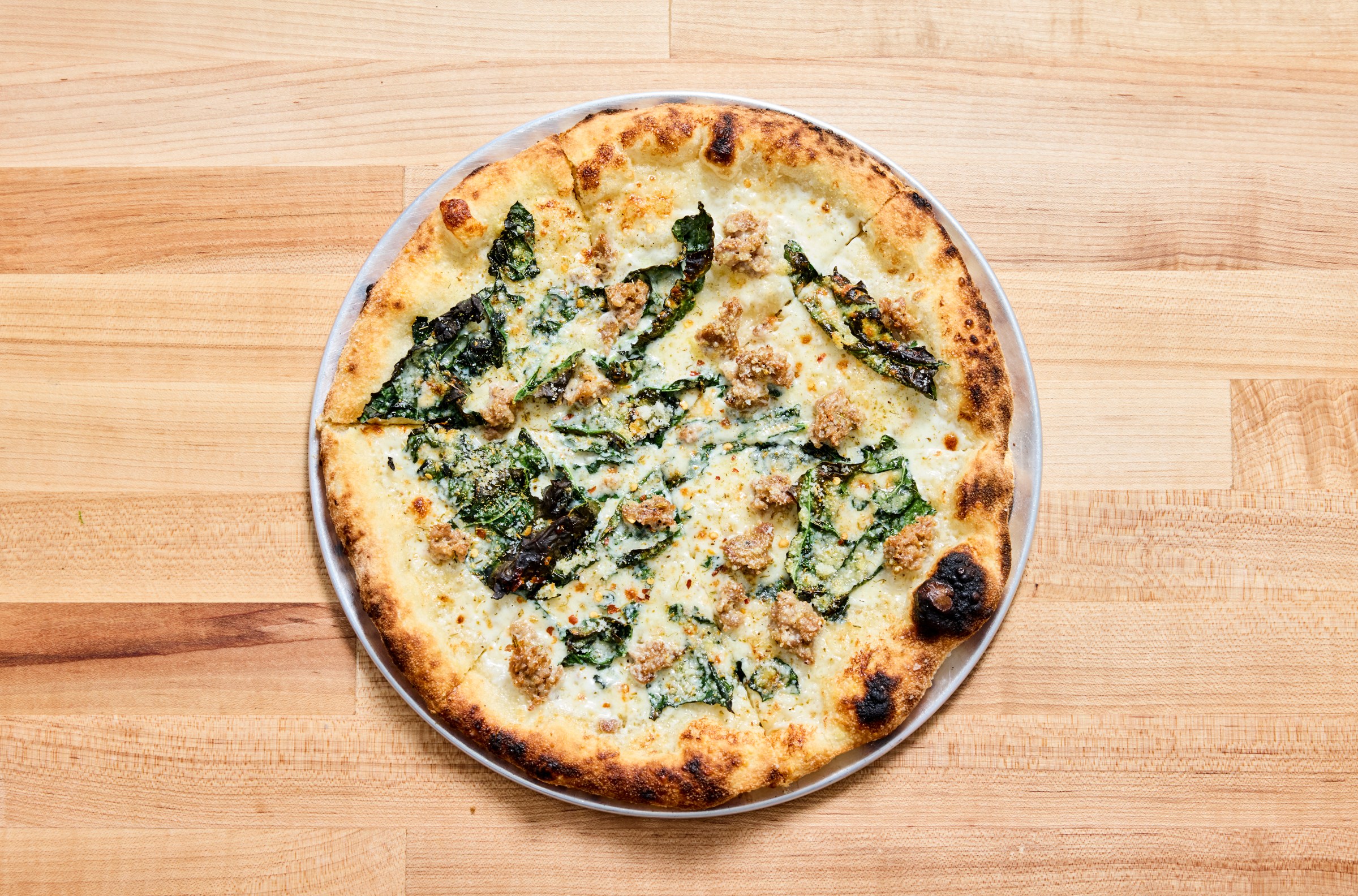 Overhead shot of fennel sausage pizza on a wood table at Fiorelli Pizza