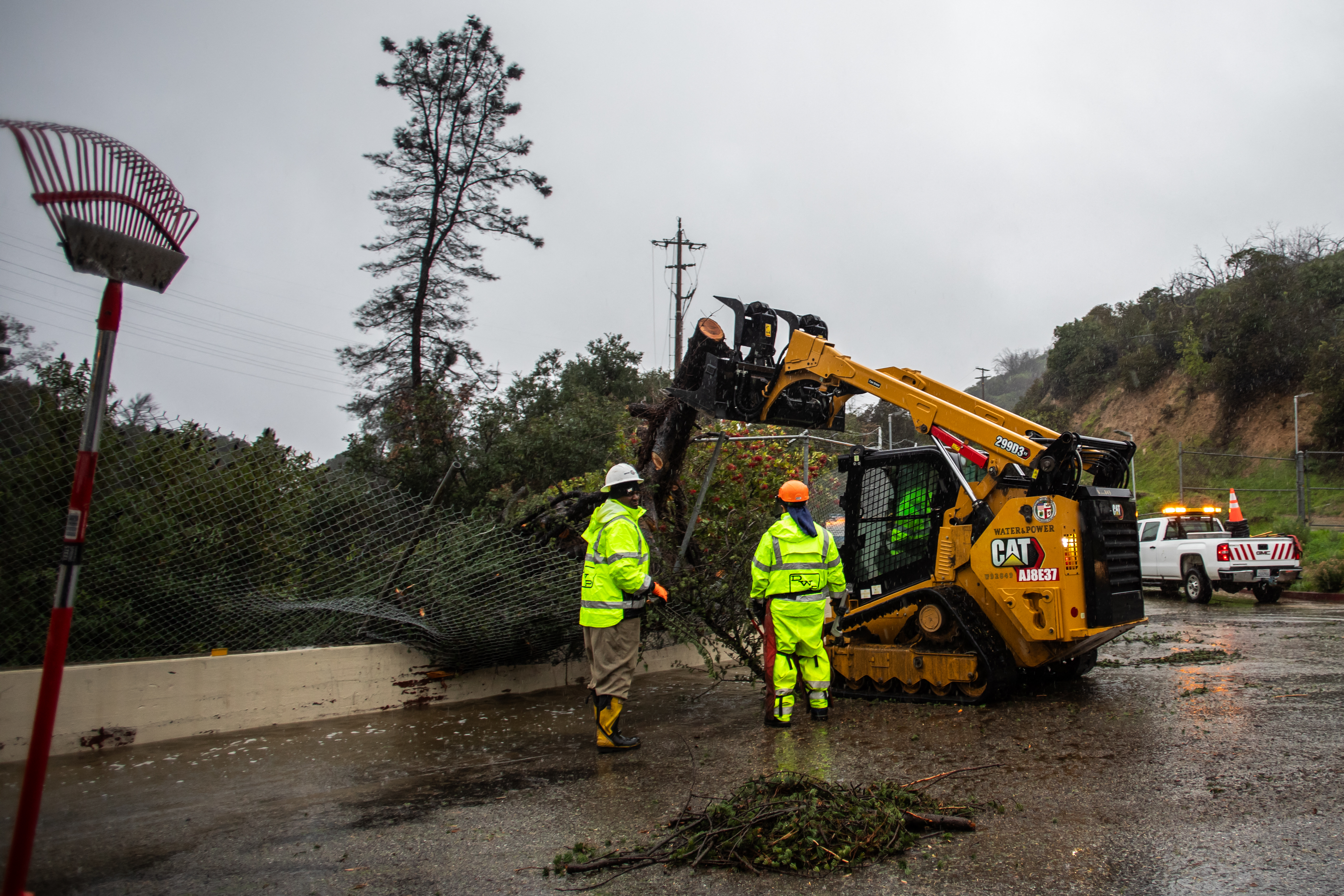 City workers try to remove a tree that felt on a wall next to the Hollywood Water Reserve on December 24, 2025 in Los Angeles, California. A major winter storm rolled into California on December 23, forcing hundreds of evacuations in burn areas while threatening flooding and travel delays through Christmas for much of the state, officials said.<br />
A “strong atmospheric river brings heavy rain, snow, and wind to California through Friday,” the National Weather Service said in a statement on December 23, warning anyone in northern, central and southern parts of the state to “exercise extreme caution.” (Photo by Apu GOMES / AFP via Getty Images)