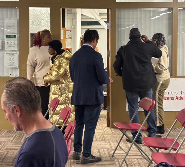 A group of people stand and talk in a room with red chairs