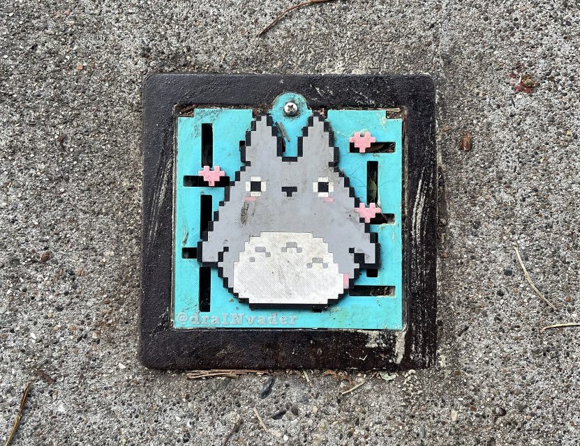 A pixel art tile depicting Totoro from "My Neighbor Totoro" is mounted on a turquoise background and set into concrete.