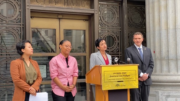 Oakland City Councilmember Janani Ramachandran speaks about proposed budget amendments at a podium on the steps in front of City Hall, alongside fellow council members Zac Unger, right, Charlene Wang, far left, and Rowena Brown. (Shomik Mukherjee/Bay Area News Group)
