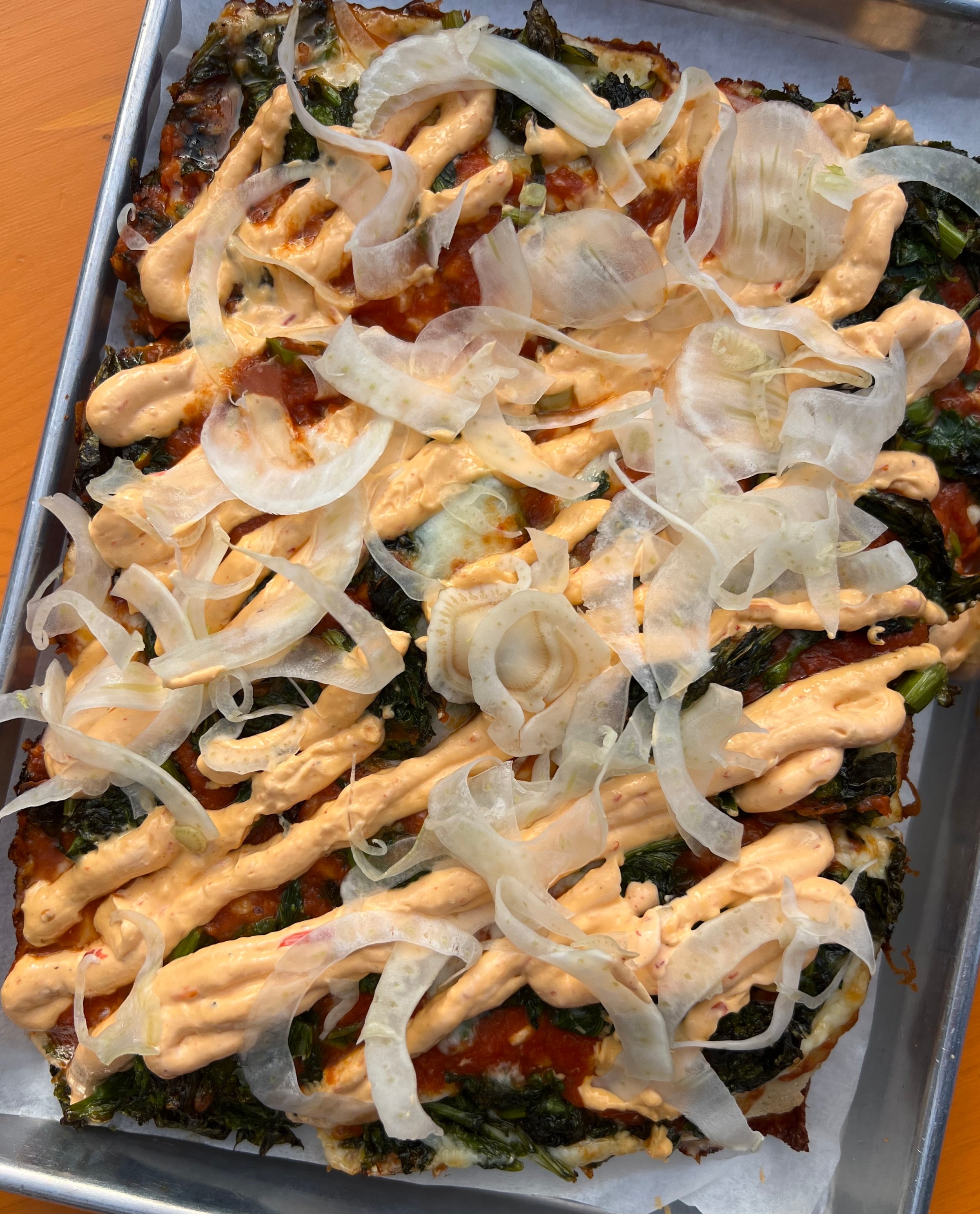 A pizza with a creamy drizzle and fronds of thinly sliced fennel. 