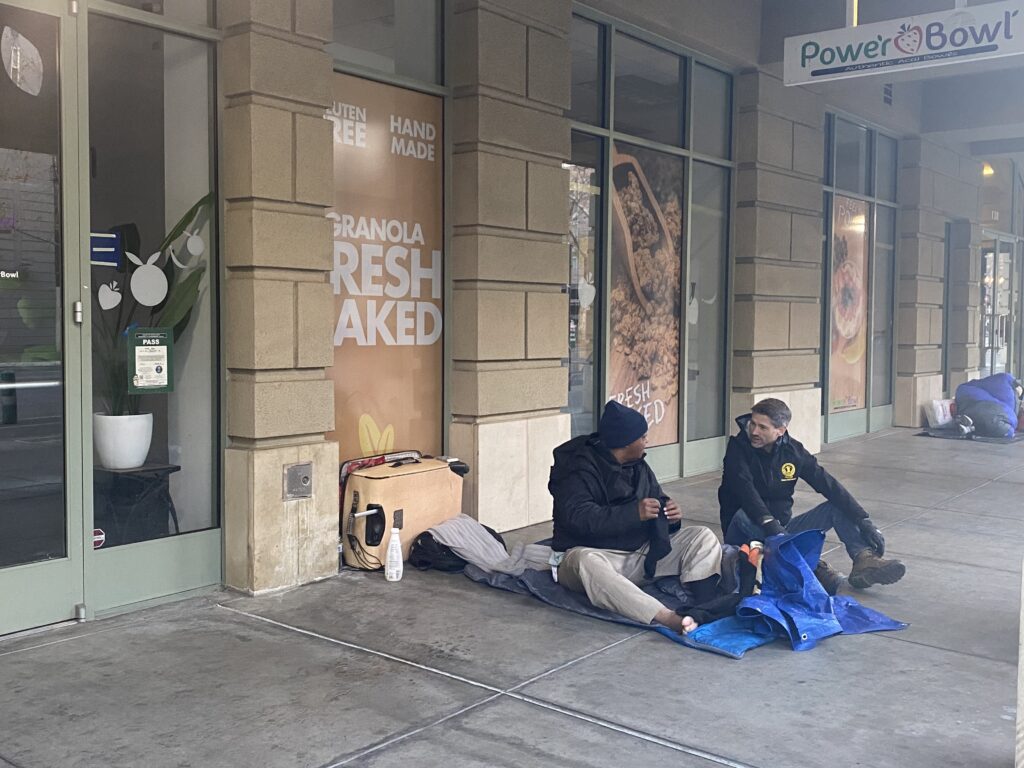 Two people sitting on the sidewalk in downtown San Jose