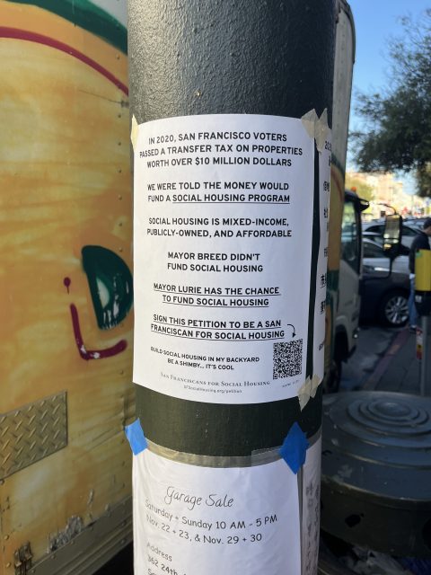 A flyer on a pole explains a tax for San Francisco social housing, urges residents to sign a petition to fund social housing, and mentions mixed-income, publicly-owned housing.
