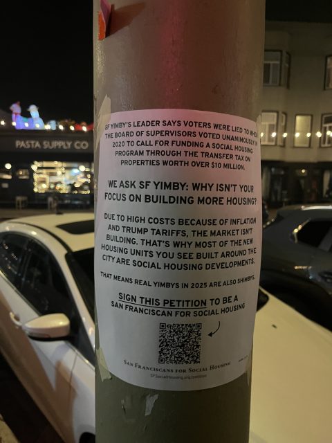 A printed flyer is taped to a street pole at night, discussing SF YIMBY, housing costs, and a petition for San Francisco social housing. Cars and a lit restaurant are visible in the background.