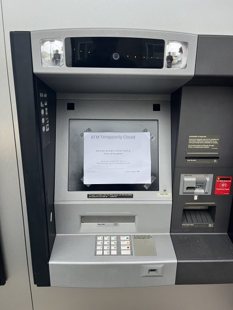 A sign reading "ATM Temporarily Closed" is taped to the screen of an out-of-service ATM. The keypad and card slot are visible below the screen.