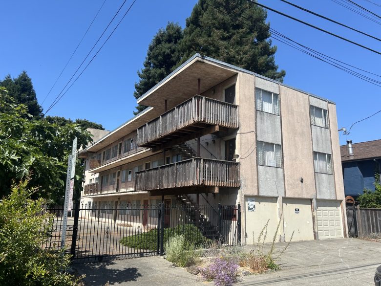 A three-story apartment building with faded paint and curtains drawn in all of its windows