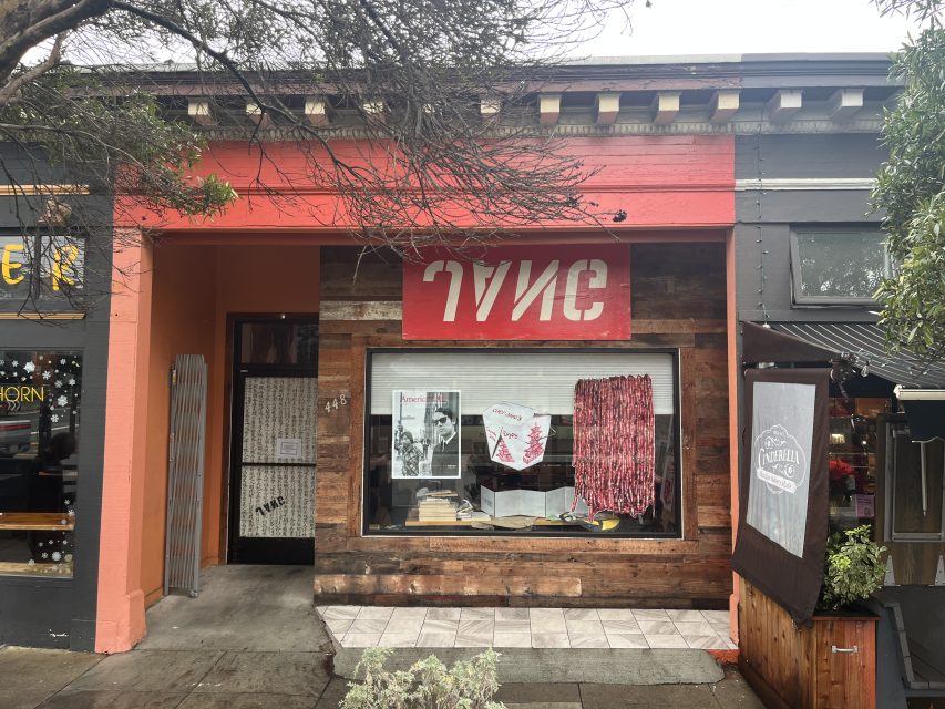Street view of the front of a store named "TYPE" with a red and white sign, wood paneling, and display items in the window, including books and patterned fabric.
