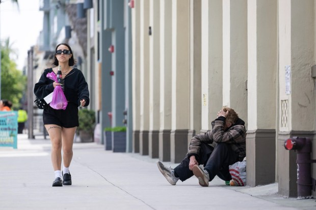 A woman walks past a homeless man on West 3rd St. in downtown Long Beach on Monday, May 12, 2025. Governor Gavin Newsom is urging California's local governments to begin clearing homeless encampments, escalating the state's efforts to ban makeshift camps on sidewalks and in parks. (Photo by Drew A. Kelley, Press-Telegram/SCNG)