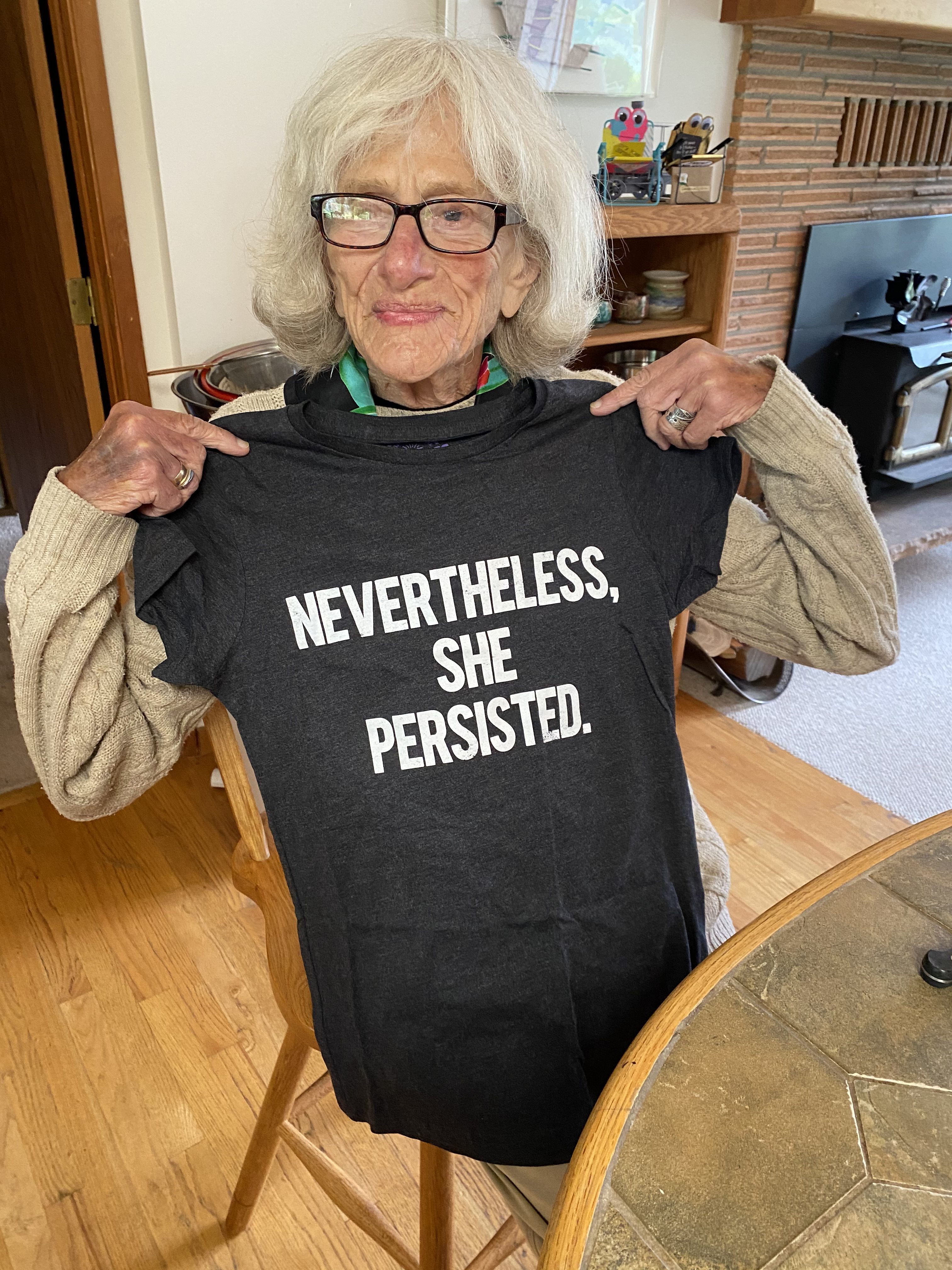 Sylvia Manheim holding up a shirt that reads, “Nevertheless, she...