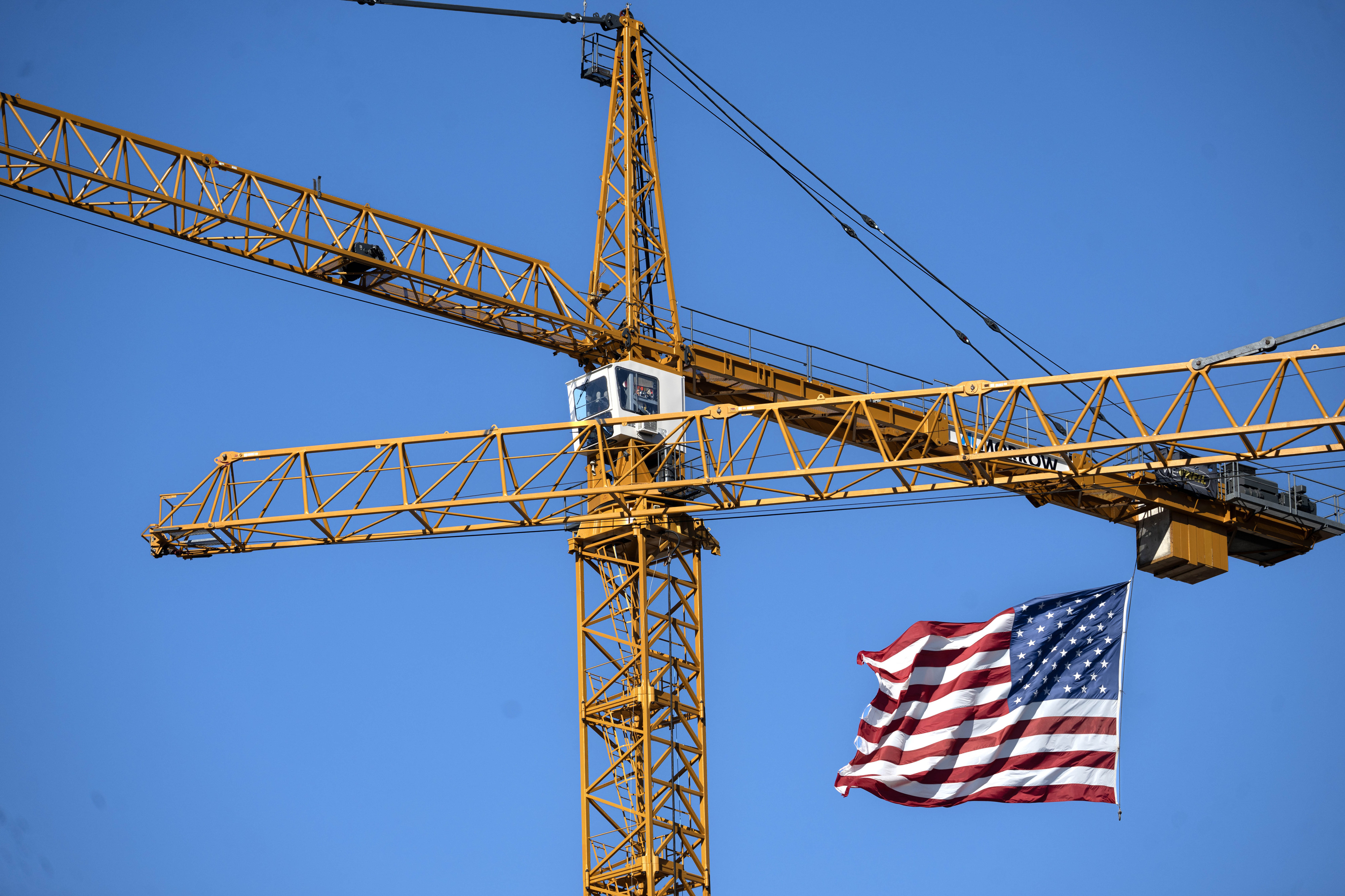 Old Glory flaps in the wind as cranes are used...