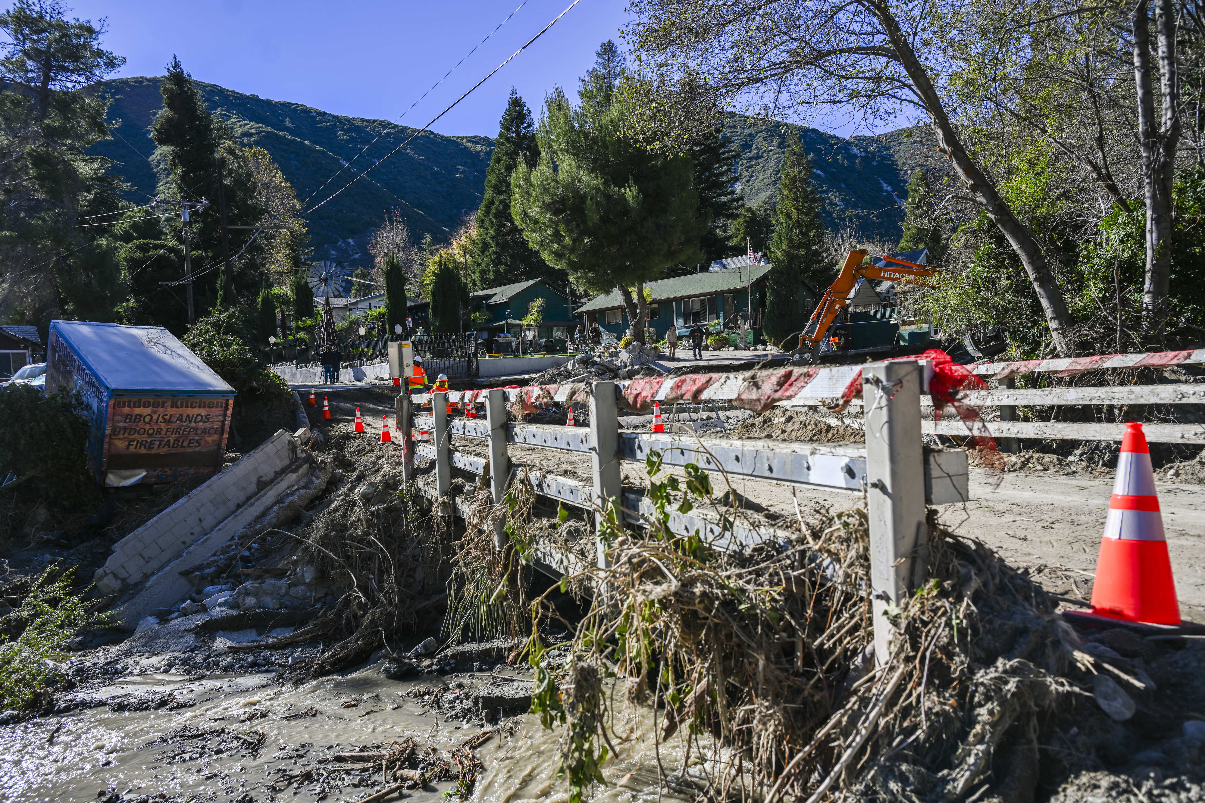 Property damage and debris line the damaged roadway and bridge...