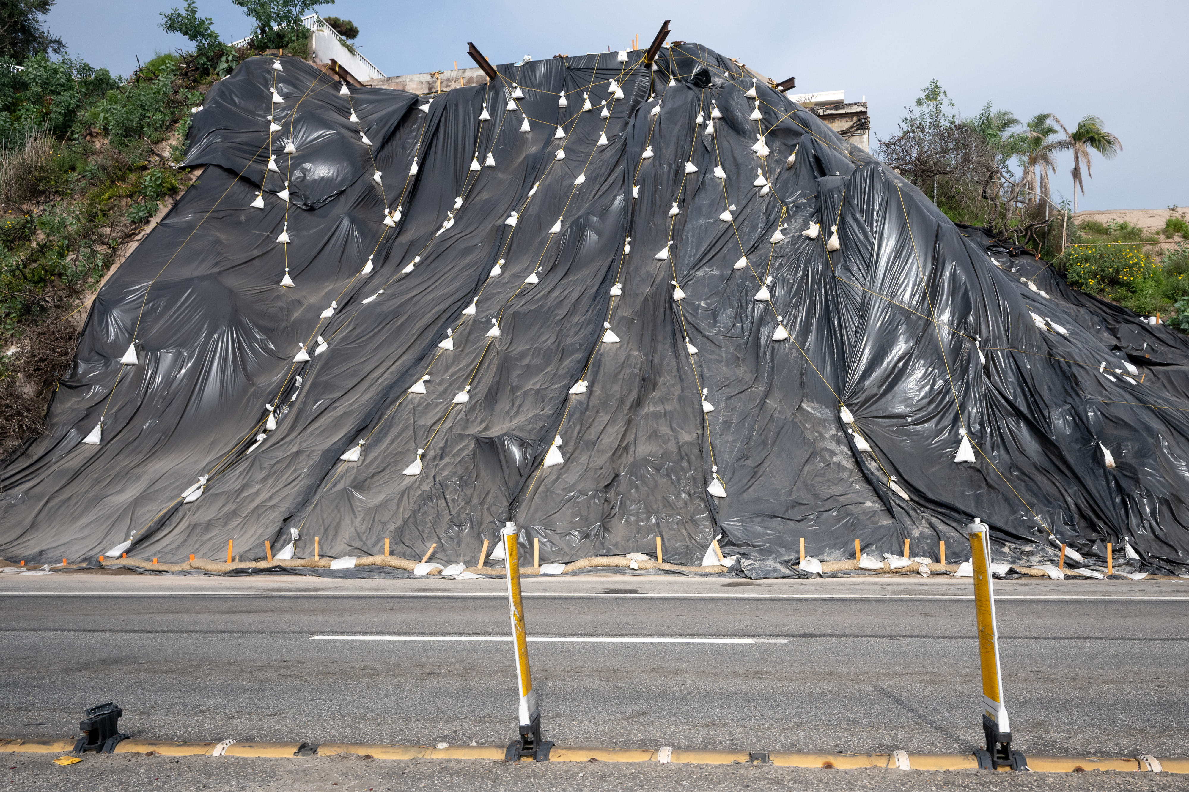 A hillside is covered with protective plastic along Pacific Coast...
