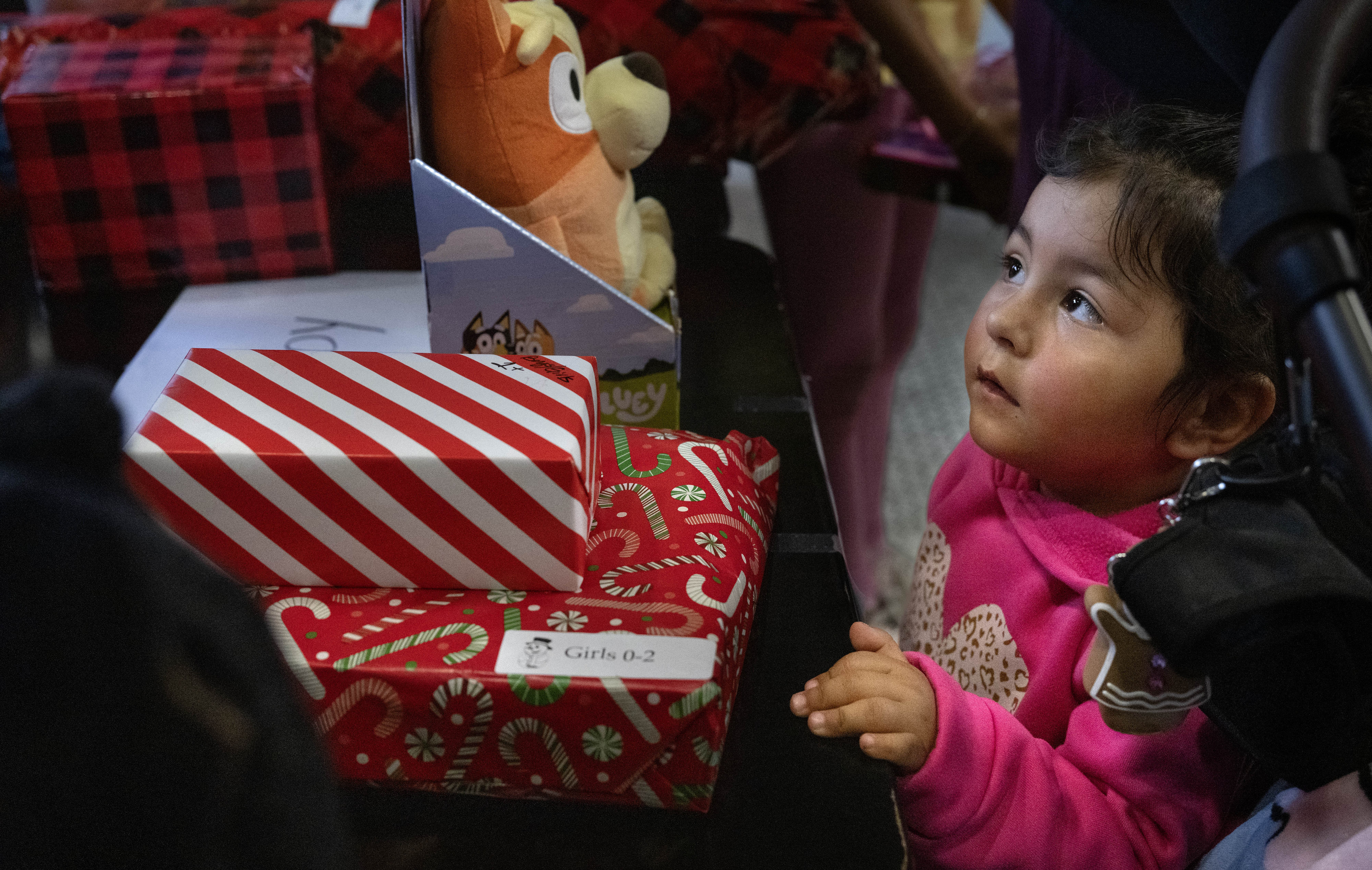 Olivia Cruz, 2, watches volunteers sort through gifts before giving...