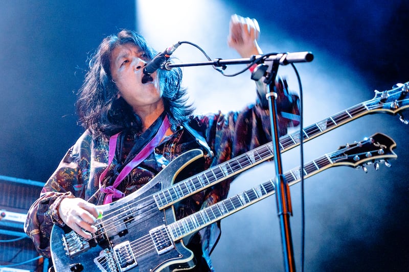 Takeshi points to the audience on stage while playing a double-neck guitar-bass.