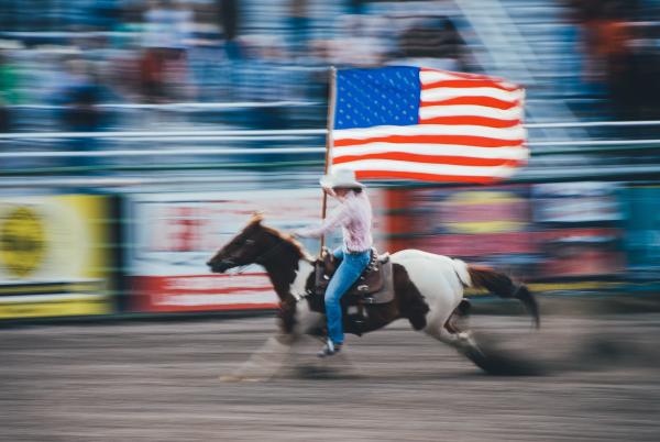 Woman riding a horse at the rodeo while holding a large American flag