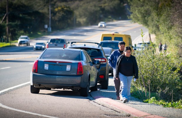 Hikers walk next to parked cars on the shoulder of state Route 67 near Mt. Woodson. Four new parking areas are designed to provide safer parking along the dangerous stretch of road. (Howard Lipin / For The San Diego Union-Tribune)