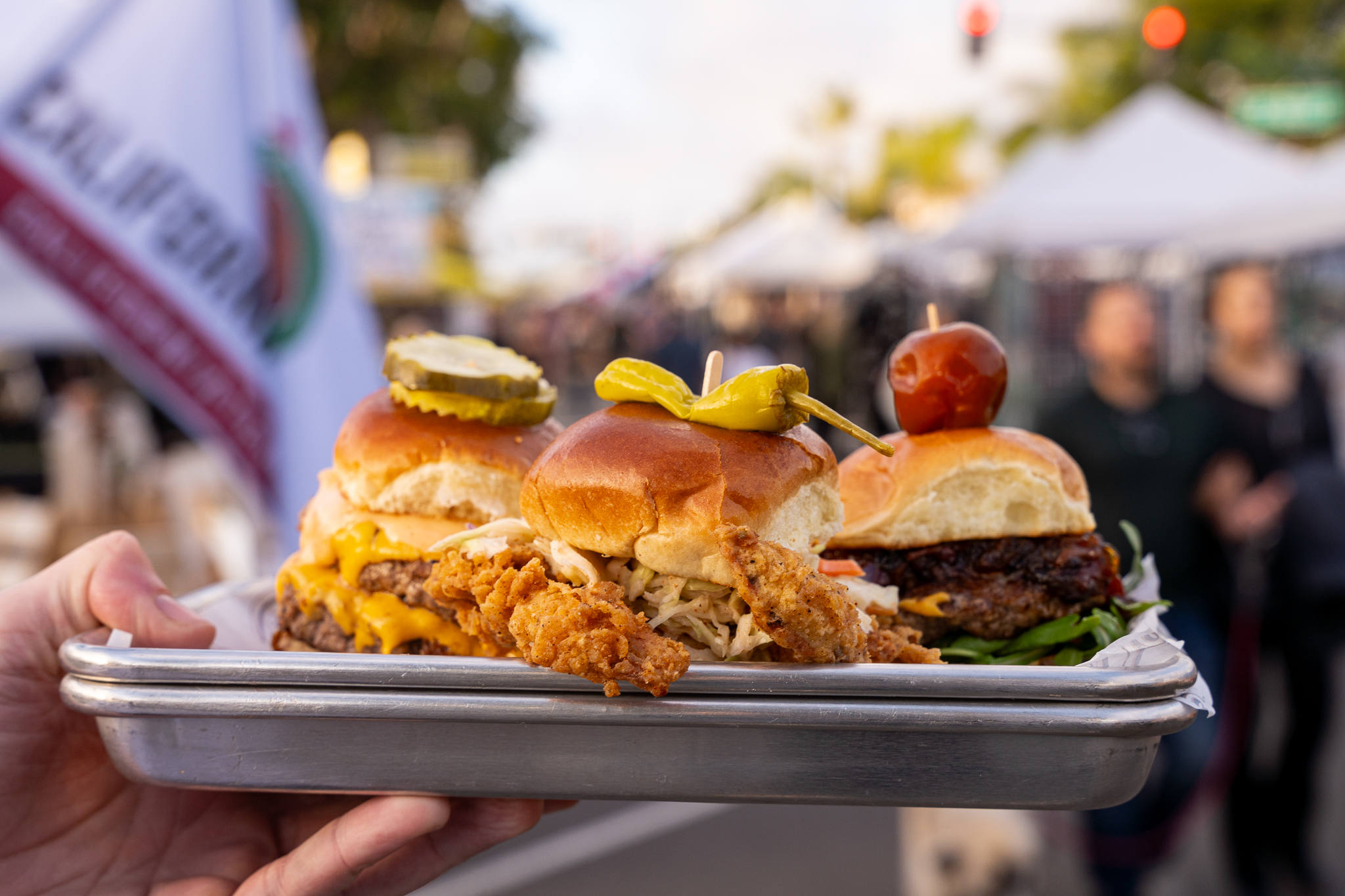 Hand holding up a tray of three sliders from Rosemarie’s Burgers.