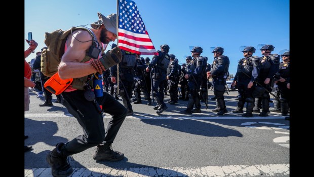 A peaceful demonstrator picks up an American flag that was lying on the ground as California Highway Patrol officers arrive in riot gear to disperse anti-immigration demonstrators protesting and blocking the entrance to U.S. Coast Guard Island, after dozens of federal agents, including personnel from U.S. Customs and Border Protection (CBP) and Immigration and Customs Enforcement (ICE), entered the island earlier in Oakland, Calif., on Thursday, Oct. 23, 2025. (Ray Chavez/Bay Area News Group)