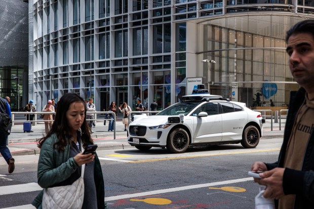 A Waymo autonomous vehicle waits at a traffic light as pedestrians walk near Salesforce Tower in San Francisco, Calif., on July 2, 2025. (Dai Sugano/Bay Area News Group)