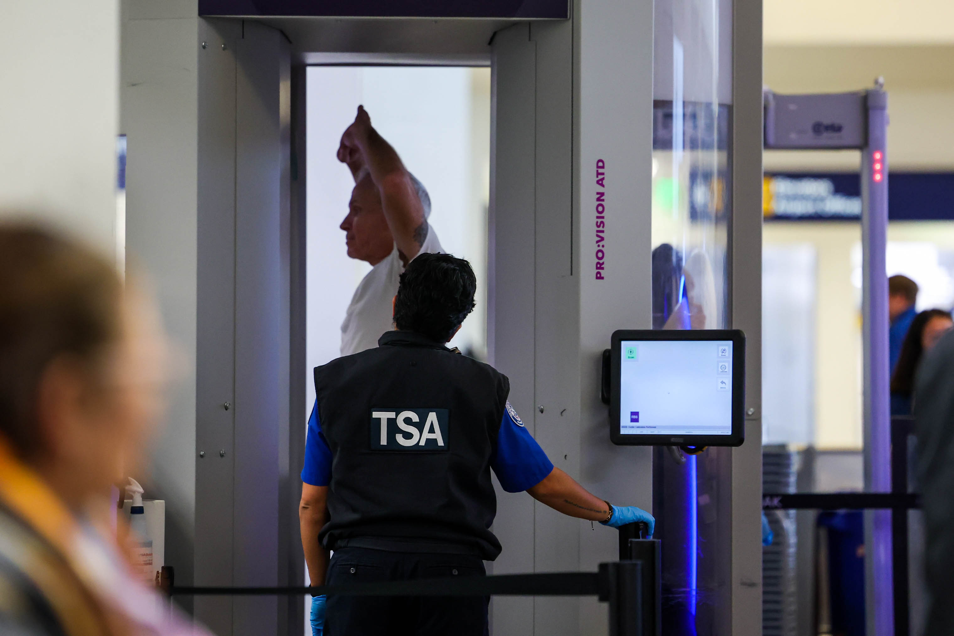A TSA agent monitors a checkpoint screening station as a...