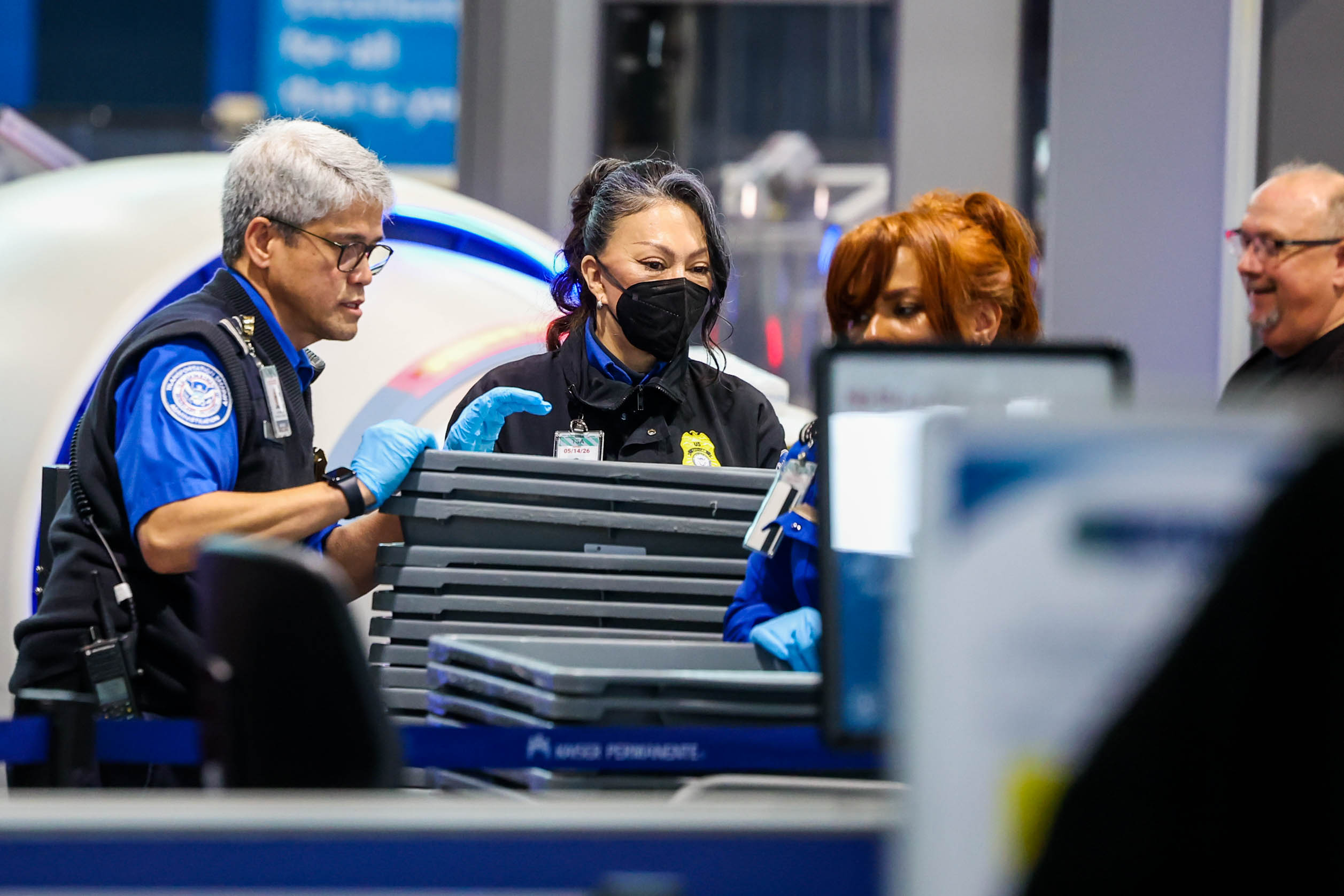 TSA agents check travelersâ luggage at a checkpoint screening station...