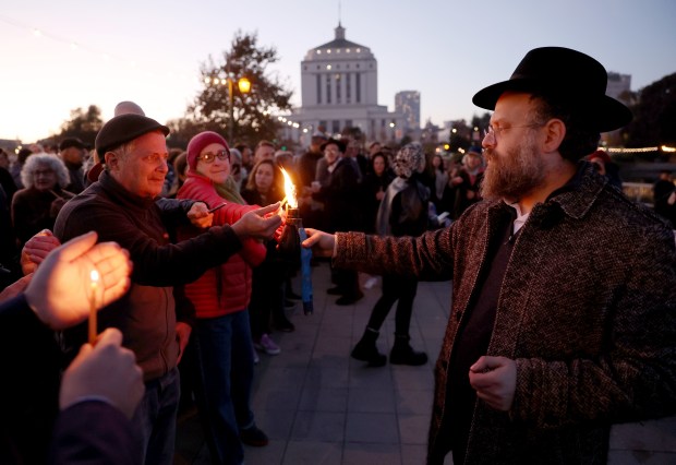 Rabbi Dovid Labkowski, of Chabad Oakland, lights candles for community members during a Hanukkah menorah-lighting ceremony at the Lake Merritt Amphitheater in Oakland, Calif., on Sunday, Dec. 14, 2025. (Jane Tyska/Bay Area News Group)