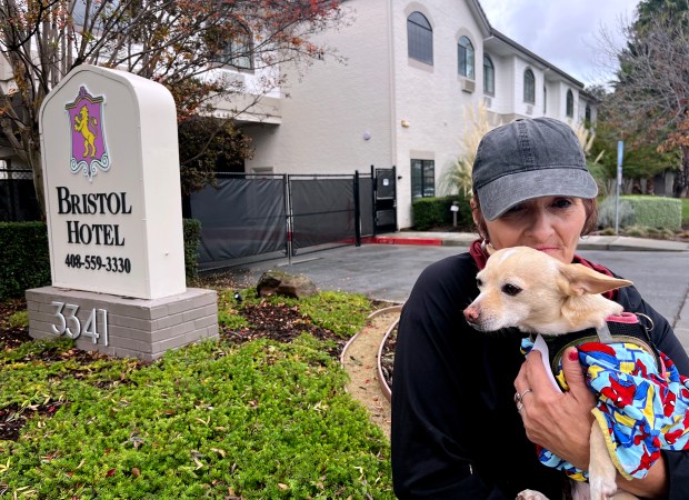 Tami Davis holds her dog Trixie outside the Bristol Hotel in Campbell, Calif., on Thursday, November 20, 2025. Davis says she is grateful for a room at the Bristol Hotel, where the city of San Jose relocated many residents of the Columbus Park homeless encampment in August. Despite the hot showers, private rooms, and chandeliers, she misses the community feeling from the encampment now that most people keep themselves locked in their rooms. (Julia Prodis Sulek/Bay Area News Group)