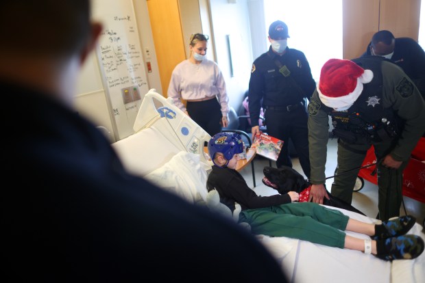 Patient Draven Jenkins visits with a dog from the Santa Clara County Sheriff's Department K-9 Unit in the children's wing of the Santa Clara Valley Medical Center on Wednesday, Dec. 17, 2025, in San Jose, Calif. The county sheriff and fire departments collected hundreds of toys from the community to be distributed at the hospital and other sites throughout the county. (Aric Crabb/Bay Area News Group)