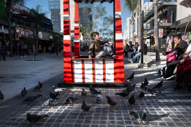 Reyna Alexandra Mendoza, 7, sits on a metal structure along Tijuana's tourist strip, Revolution Avenue, on December 6, 2025, in Tijuana, Mexico.The city government recently closed traffic on three blocks of Revolution Avenue in order to convert the street into pedestrian walkways and mini plazas with trees and sitting areas. (David Maung / For The San Diego Union-Tribune)