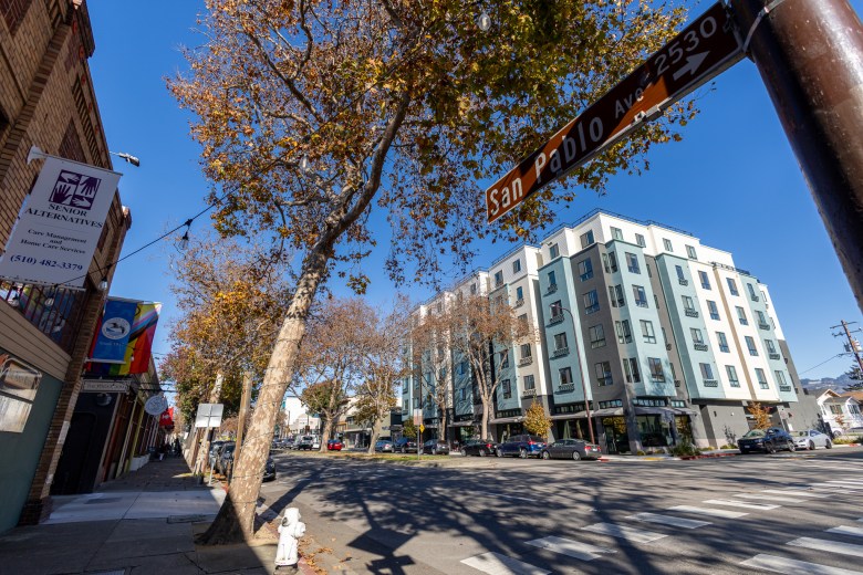 A view across San Pablo Avenue, where a new six-story apartment building stands opposite an older line of brick storefronts