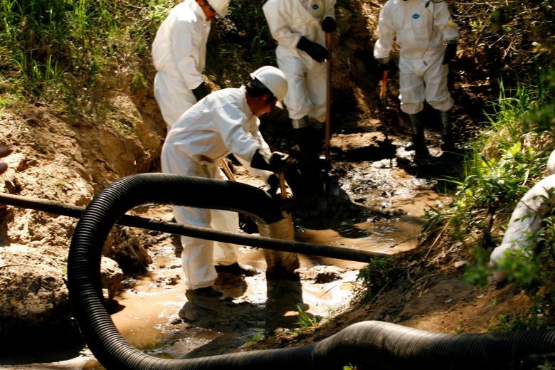 Workers in protective suits cleaning oil from a waterway using tools.