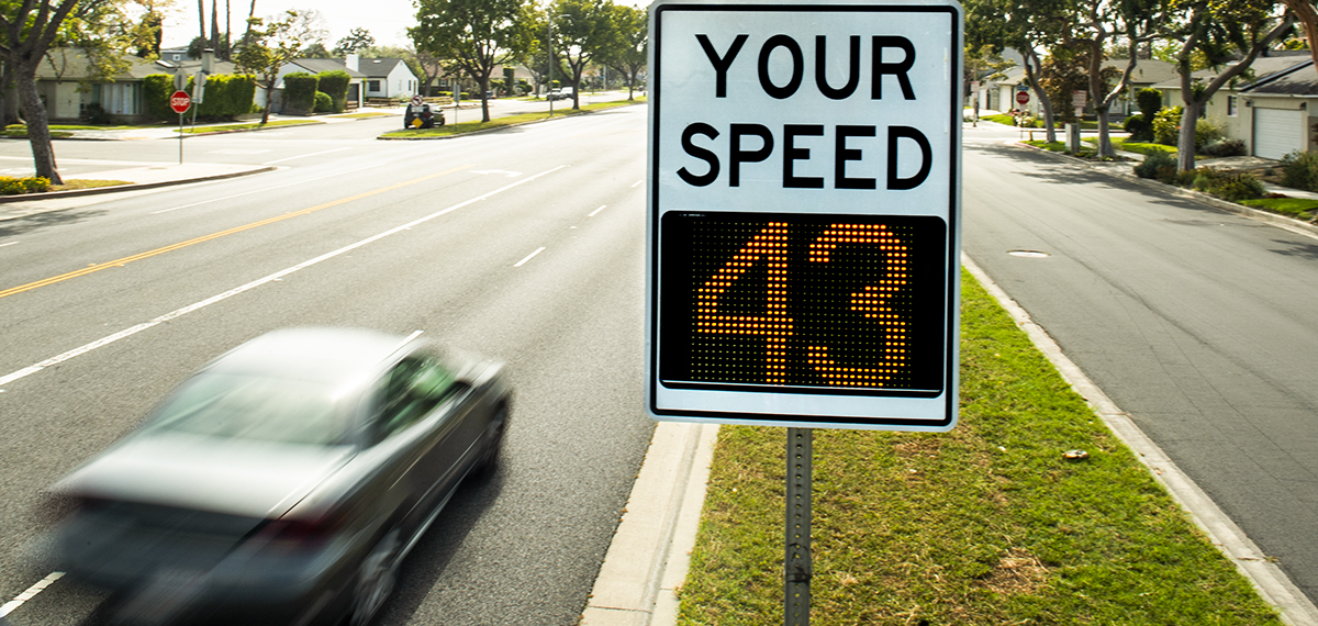 A vehicle zooms past a radar speed display sign.