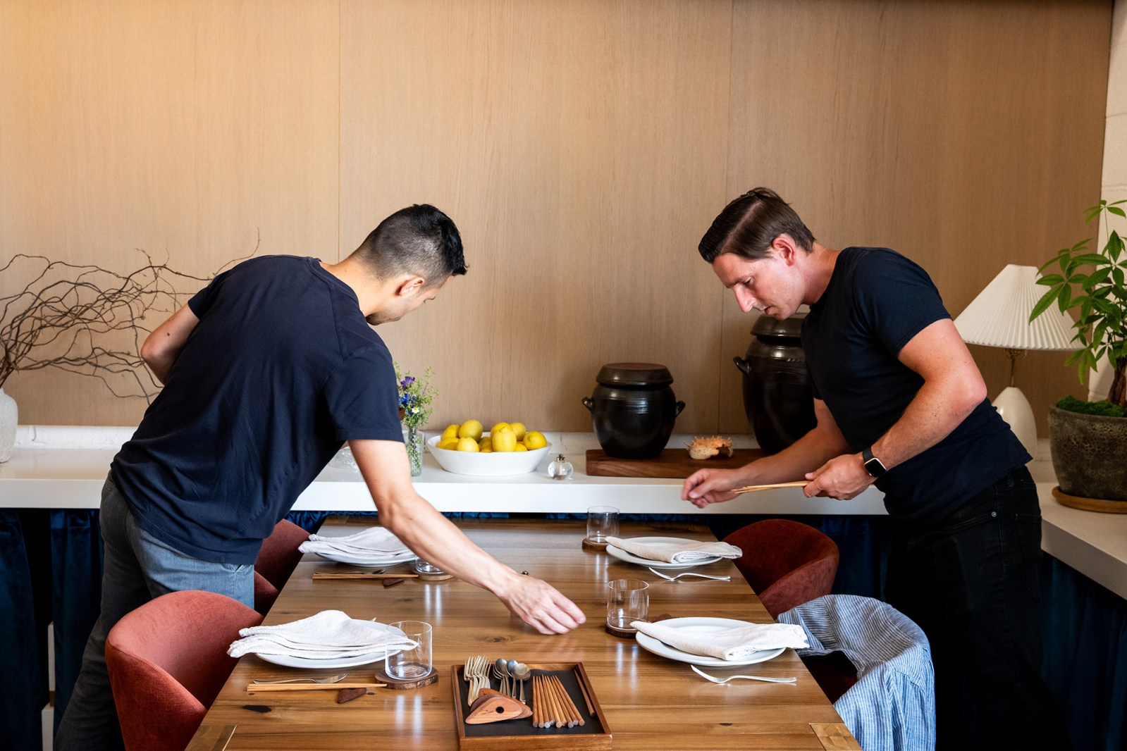 Two people carefully set a table at a minimalist, fancy restaurant.