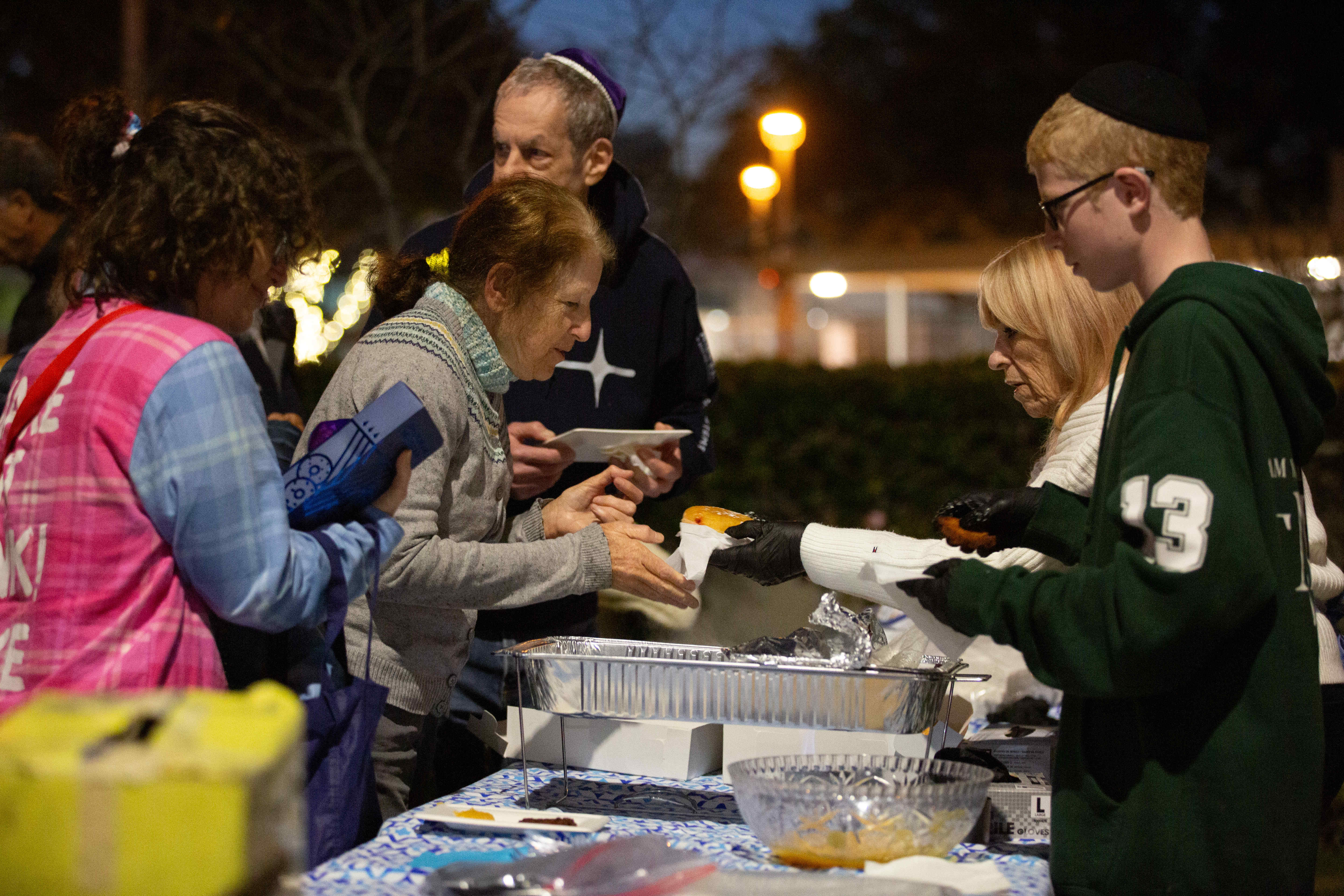 A woman is served a donut during a menorah lighting...