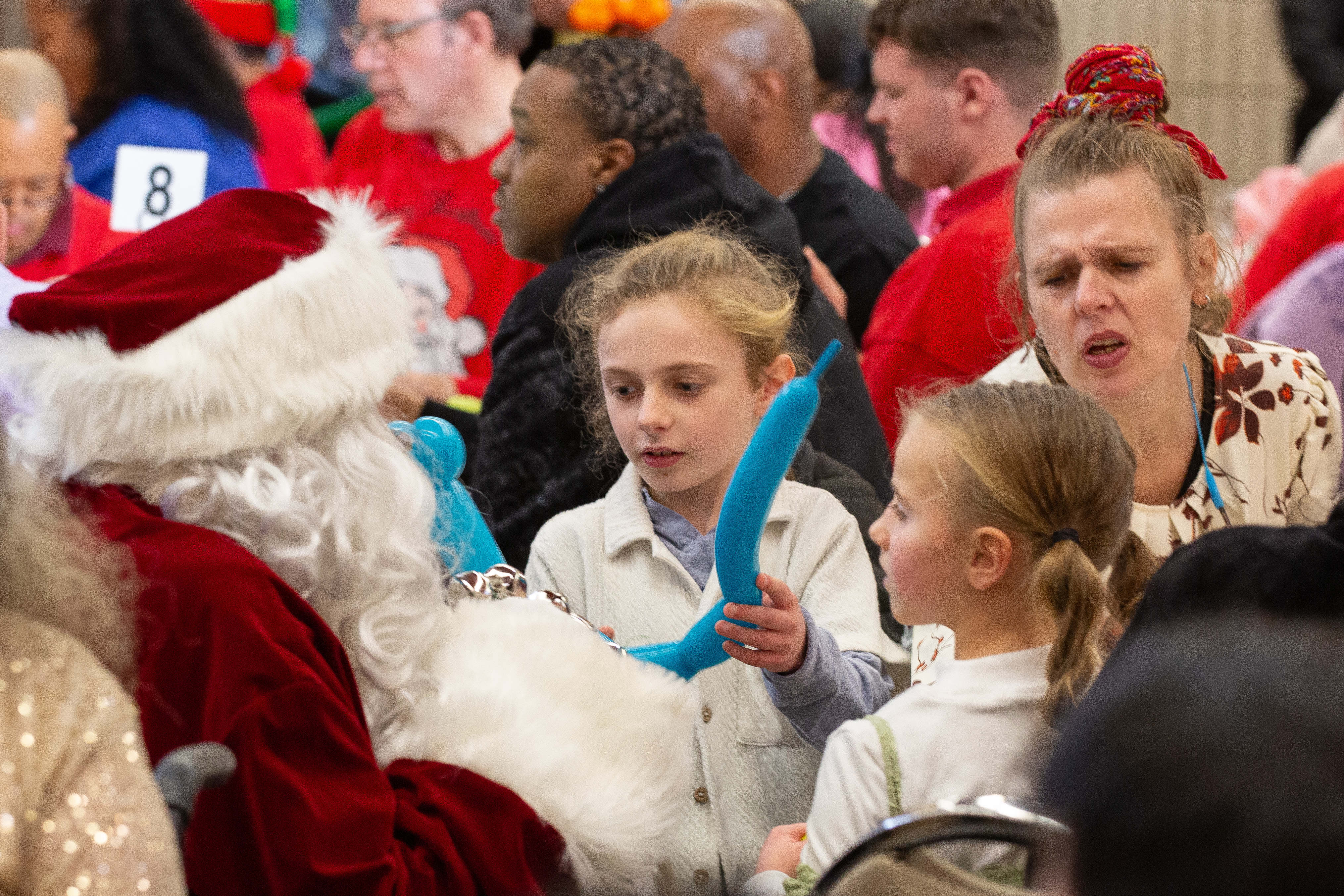Two girls show Santa Claus a balloon animal during the...