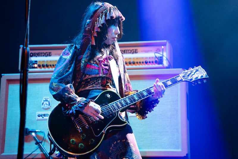 Wata, in a layered gothic lolita style dress and headdress, playing guitar in the spotlight.
