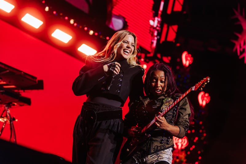 Reneé Rapp in all-black suit and guitarist in green jacket with denim shorts playing guitar.