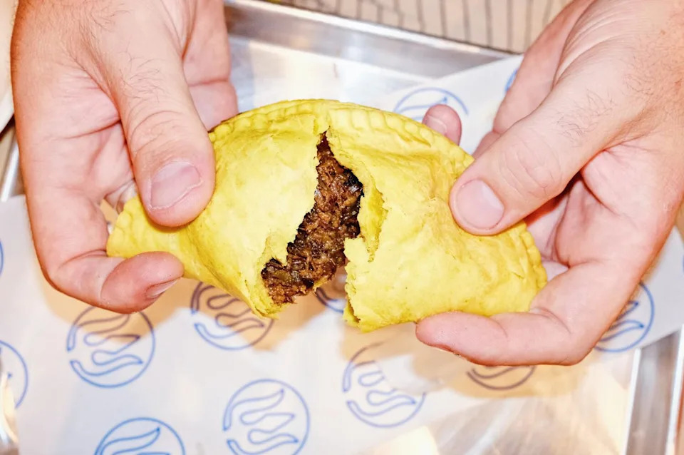 Two hands rip an oxtail patty in half, the crust yellow, the meat inside shredded at Bridgetown Roti in East Hollywood