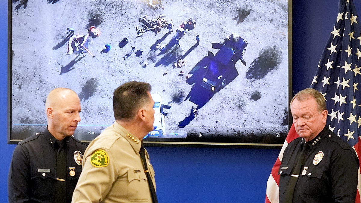 Two senior law enforcement officials speak beside large aerial images during an investigation update in Los Angeles.