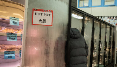 A person wearing a dark coat stands partly inside a foggy glass freezer door labeled "HOT POT" in a grocery store. Shelves of packaged food are visible to the left.