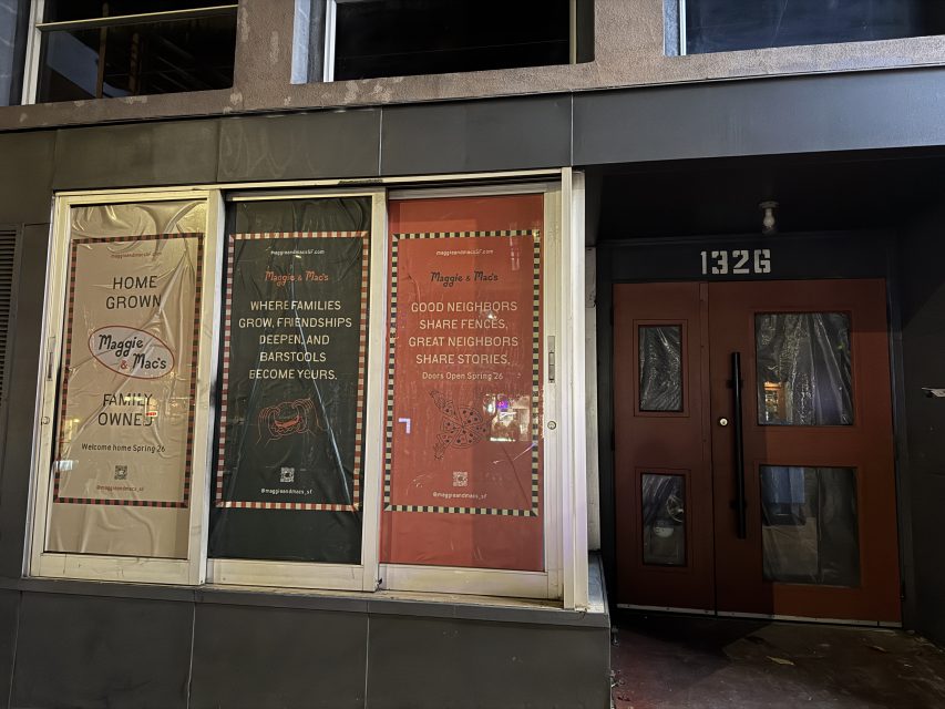 Storefront at 1326 with three large posters promoting Maggie + Macs, featuring messages about family, friendship, and neighbors, next to a red double door entrance.