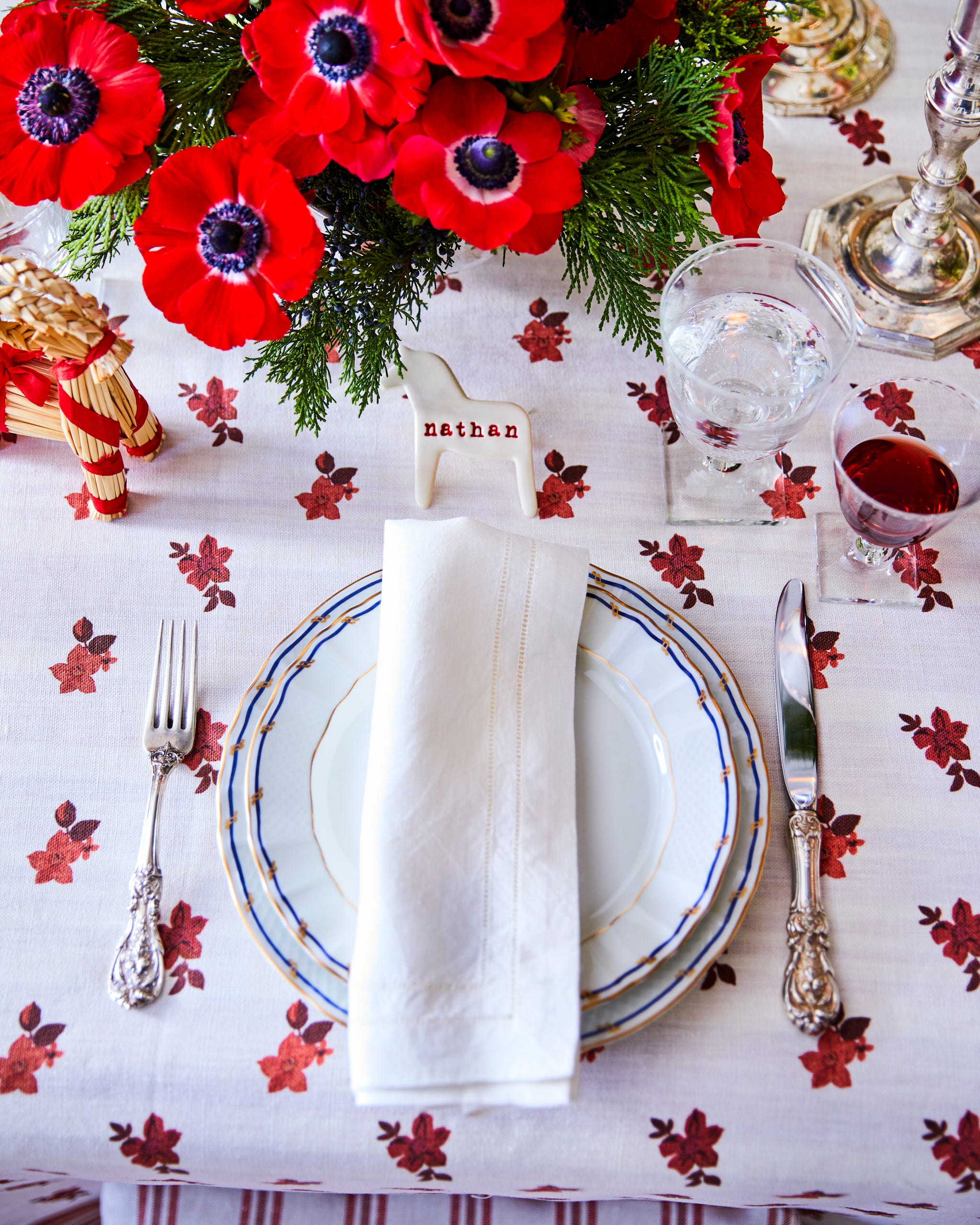 table setting with white plates on a white tablecloth with red flowers and a centerpiece of red flowers