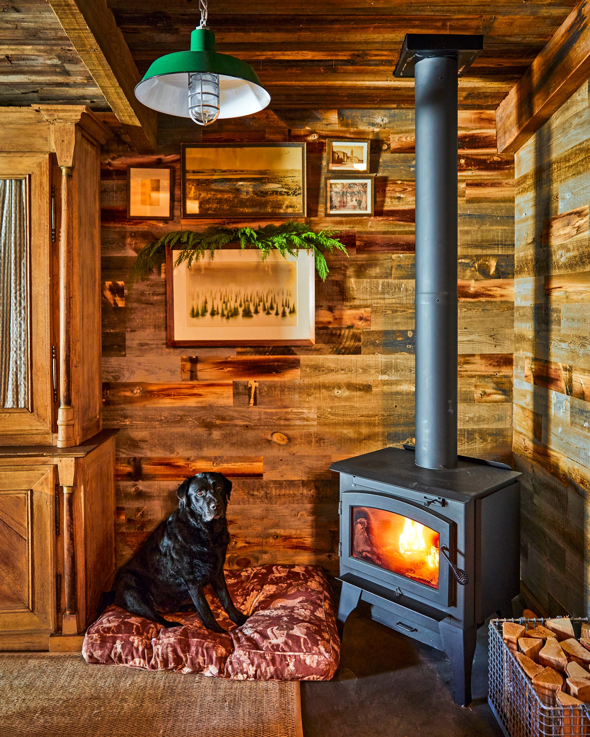 corner of living room with wood paneled walls with a black wood burning stove and a black lab sitting next to it