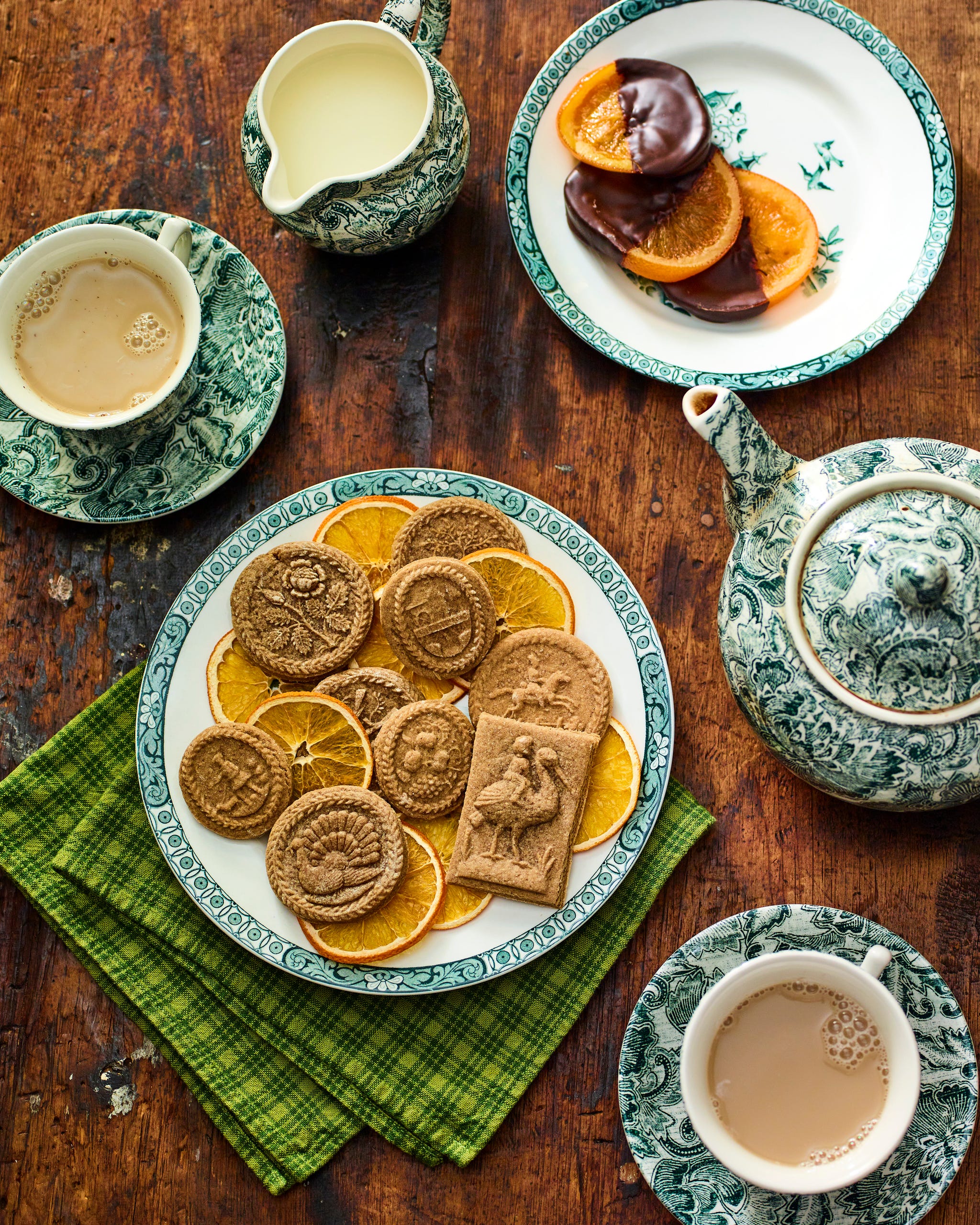 cookies made with holiday molds on a plate on a table with cups of coffee and other dishes