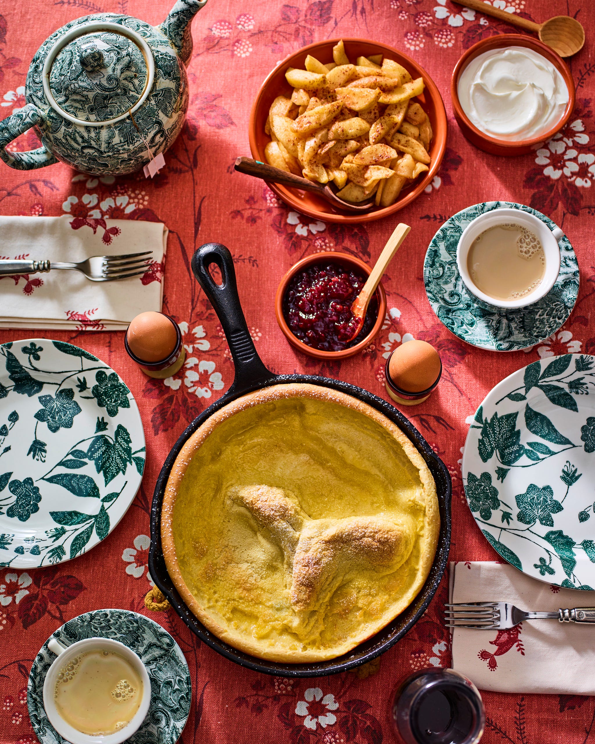 dutch baby in a pan with plates and cups of coffee and assorted toppings