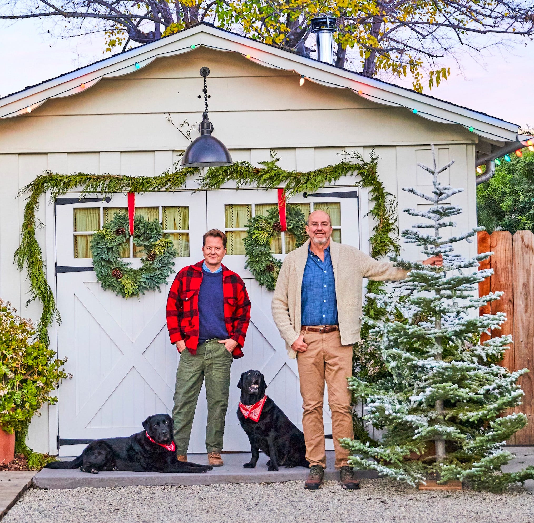 portrait of two men standing in front of a garage with a christmas tree and two black labs