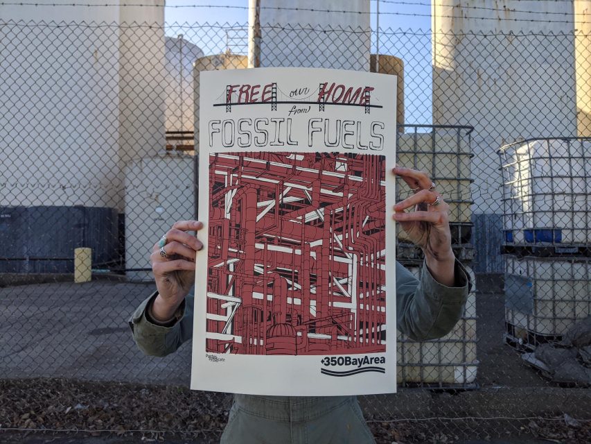 Person holding a poster that reads "Free our home from fossil fuels" with an abstract red design, standing in front of a fence and large industrial tanks.